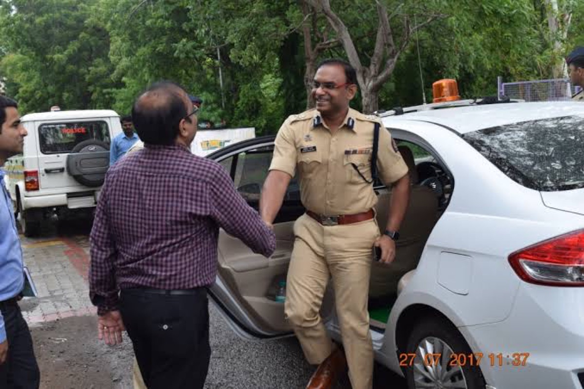 Milind Bharambe in uniform stepping from a vehicle on a field visit and greeting people, with police vehicles in the background.