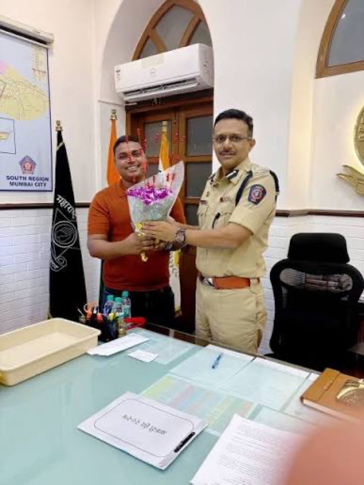 Milind Bharambe in uniform presenting a bouquet to a young man in an office of the South Region, Mumbai City police.