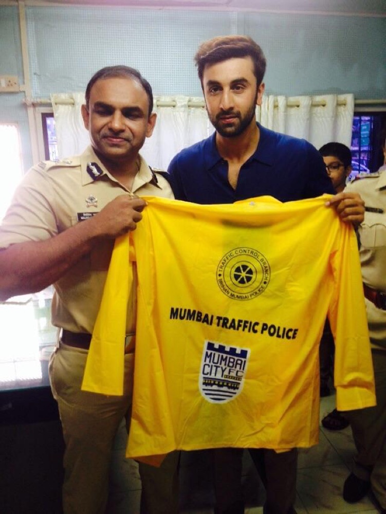 Milind Bharambe in uniform holding up a Mumbai Traffic Police jersey alongside a guest at a public road safety campaign event.