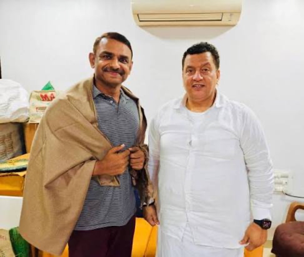 Milind Bharambe in civilian clothing, wearing a shawl presented to him, standing with a member of the public at an informal gathering.