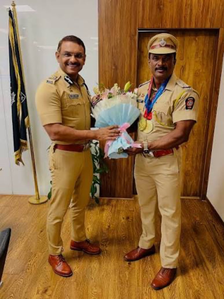 Milind Bharambe in uniform presenting a bouquet to a decorated police officer wearing medals, in an office setting.