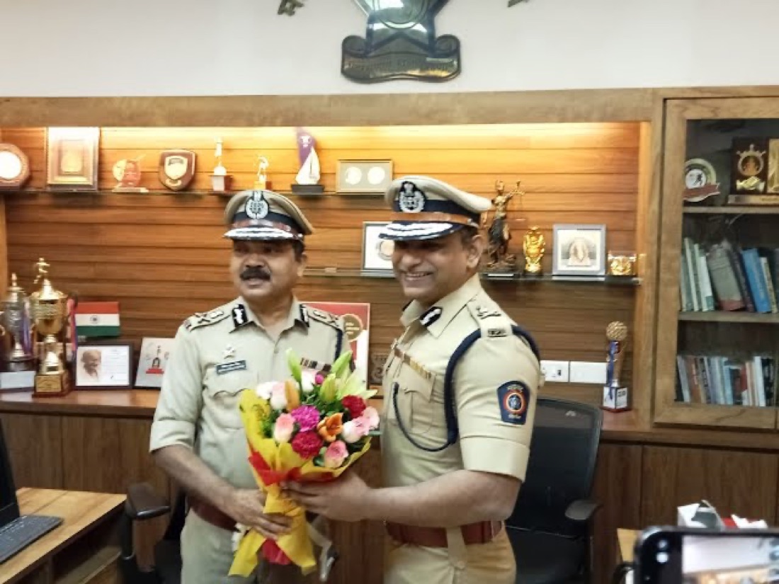 Milind Bharambe in uniform with another senior Indian Police Service officer, both holding a bouquet, in an office displaying trophies and awards.
